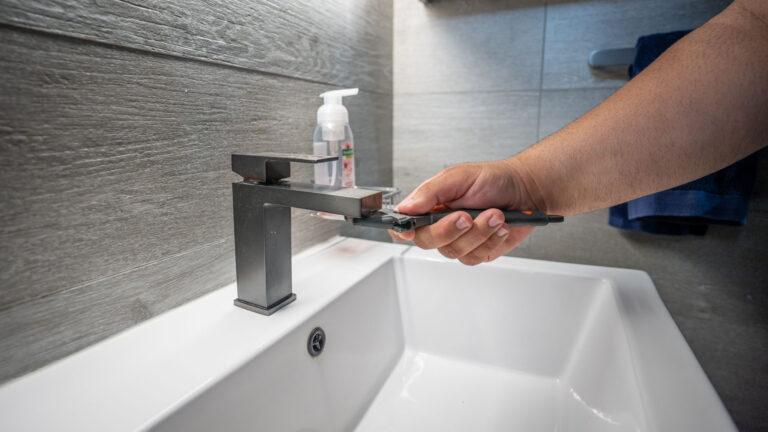 A plumber from Anton's Plumbing uses a wrench to fix a bathroom faucet, providing expert leaking tap repair services.